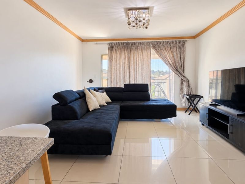 A bright and spacious living room featuring polished porcelain floor tiles, crown molding, and a sliding glass door leading to an outdoor area.