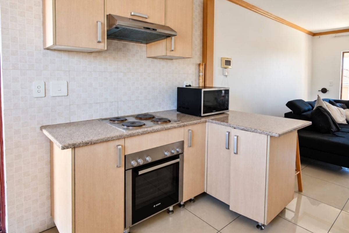 Compact kitchen featuring light wood-finish cabinetry, granite countertops, built-in oven, electric hob, and extractor fan, seamlessly integrated into an open-plan living area.