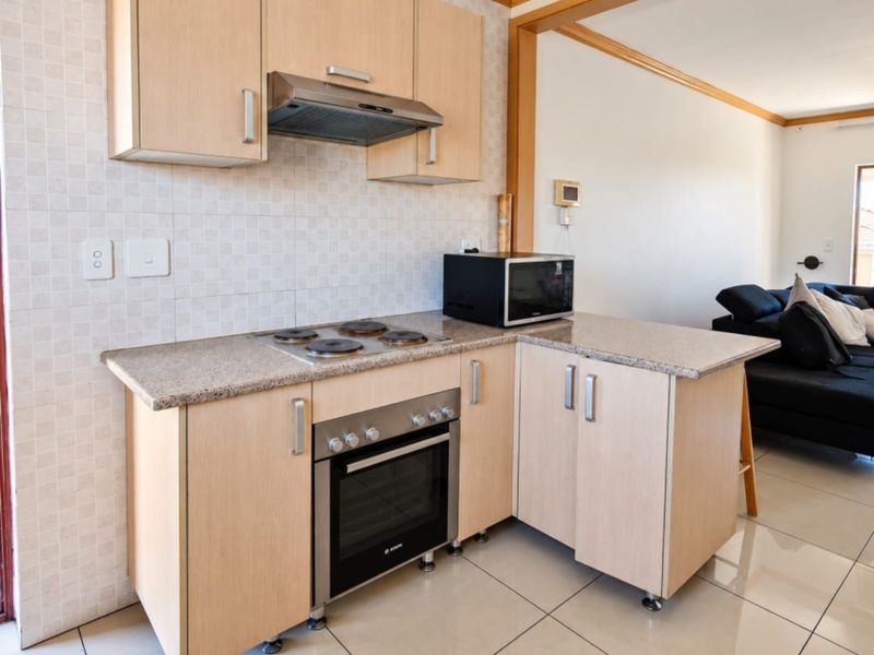 Compact kitchen featuring light wood-finish cabinetry, granite countertops, built-in oven, electric hob, and extractor fan, seamlessly integrated into an open-plan living area.