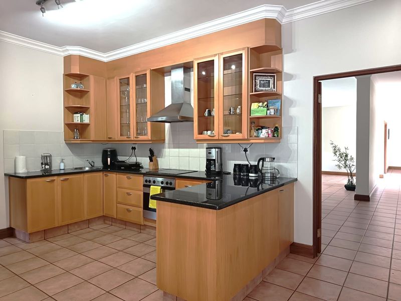 A functional kitchen featuring light wood cabinetry, black granite countertops, integrated stainless steel appliances, and tiled flooring with a seamless flow to adjacent living areas.