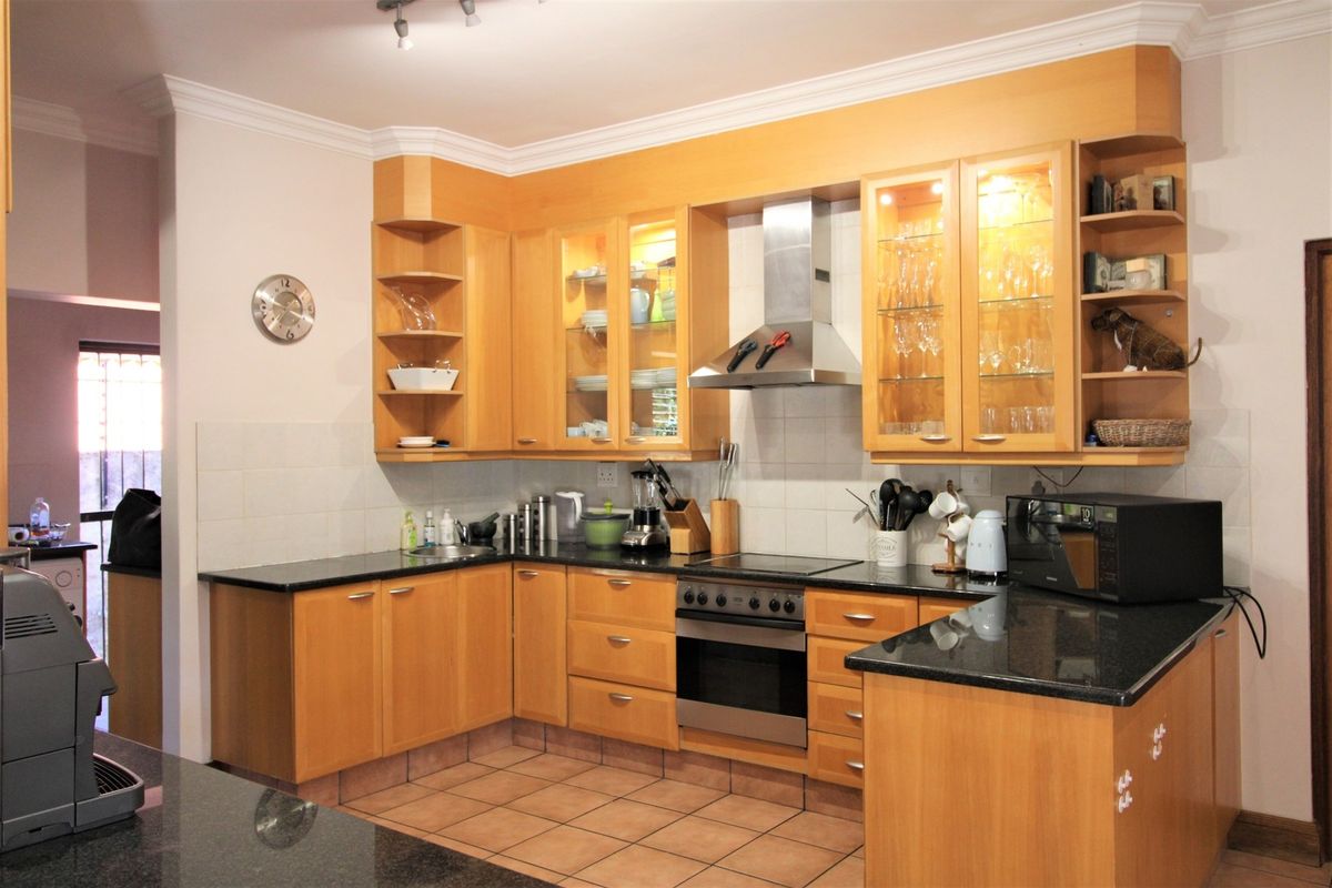 A functional kitchen featuring warm wooden cabinetry, granite countertops, integrated stainless steel appliances, and tiled flooring with a classic backsplash.