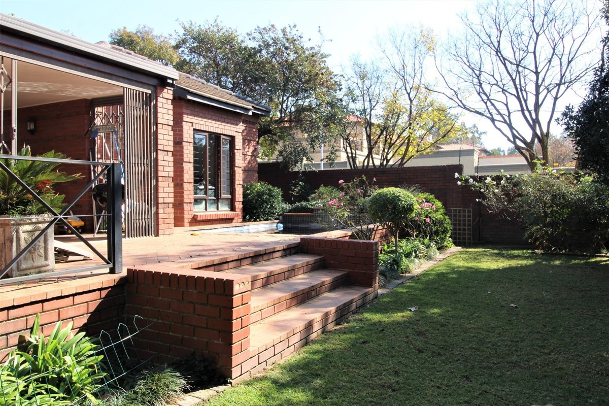Rear exterior view featuring a brick patio with stairs leading to a garden and swimming pool area, enclosed by a brick boundary wall.