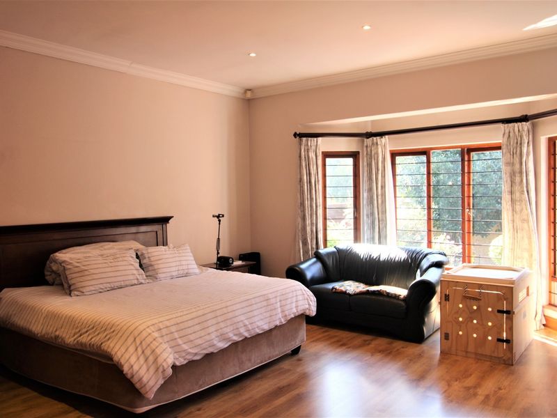 Spacious bedroom featuring laminate flooring, recessed downlights, and a large bay window with security bars, offering a bright and comfortable living space.