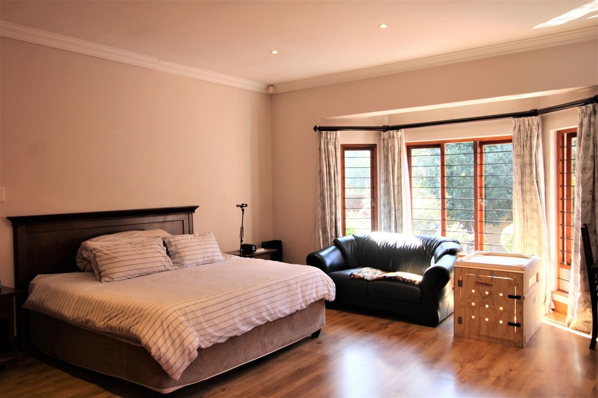 Spacious bedroom featuring laminate flooring, recessed downlights, and a large bay window with security bars, offering a bright and comfortable living space.