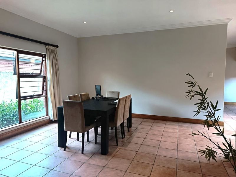 A dining room featuring neutral walls, tiled flooring, and a large window providing natural light.