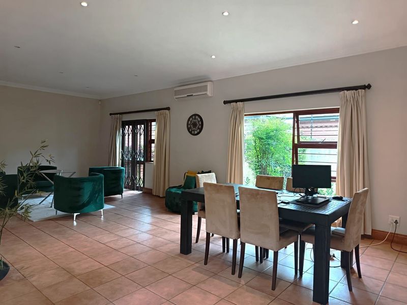 Spacious open-plan living and dining area featuring tiled flooring, recessed downlights, and an air conditioning unit, with direct access to the exterior.