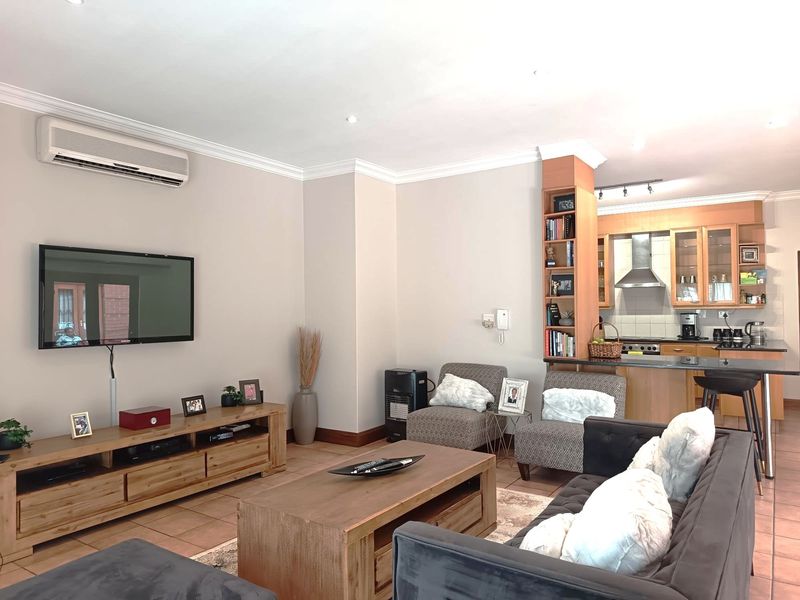 Spacious open-plan living area featuring tiled floors, a split-system air conditioner, and a functional kitchen with built-in cabinetry and an island breakfast bar.