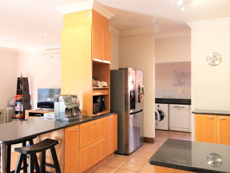 Open plan kitchen featuring granite countertops, wooden cabinetry, and an adjoining scullery area with laundry facilities, finished with tiled flooring and recessed lighting.
