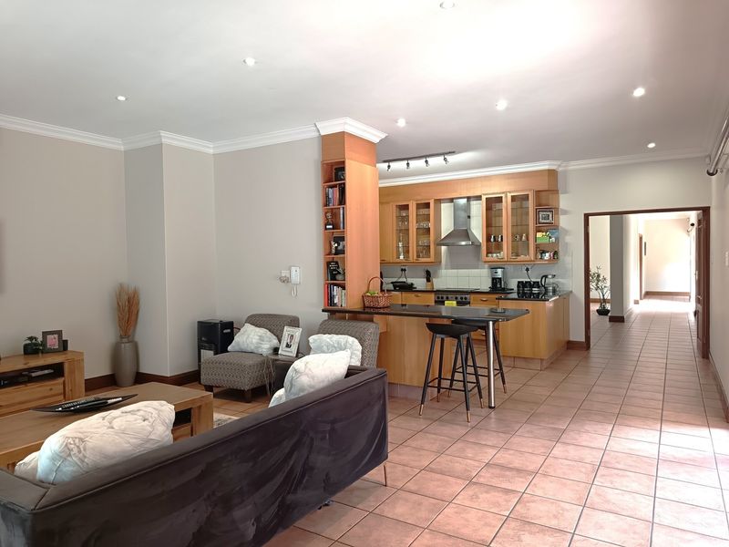 Spacious open-plan living and kitchen area featuring tiled floors, wooden cabinetry, a breakfast bar, and recessed lighting, creating a functional and connected living space.