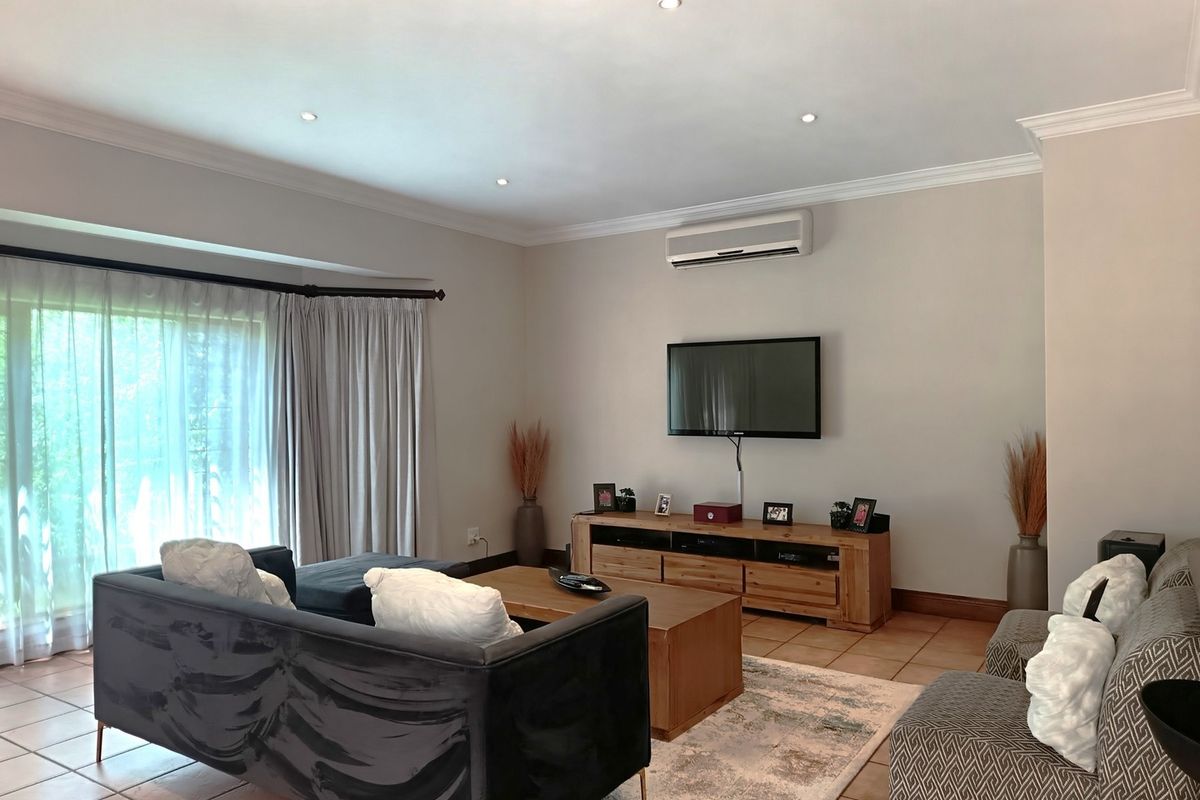 Spacious living room featuring tiled flooring, recessed downlighting, crown molding, and a wall-mounted split-system air conditioner with access to a sliding glass door.