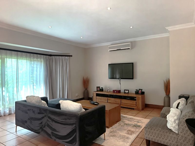 Spacious living room featuring tiled flooring, recessed downlighting, crown molding, and a wall-mounted split-system air conditioner with access to a sliding glass door.