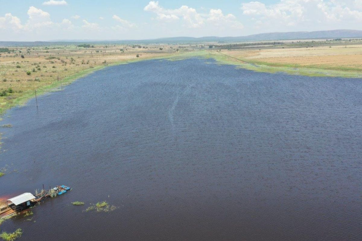 An aerial view of a large farm dam with a small jetty structure on the water's edge, surrounded by open veld landscape.