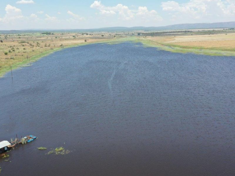 An aerial view of a large farm dam with a small jetty structure on the water's edge, surrounded by open veld landscape.