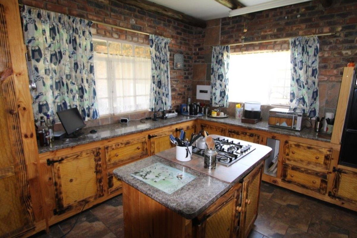 Rustic kitchen featuring exposed brick walls, wooden cabinetry, granite countertops, a central island with a built-in gas hob, and tiled flooring.