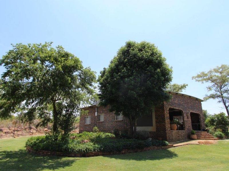A view of the rear elevation of a face brick farm house featuring a covered patio and established garden surroundings.