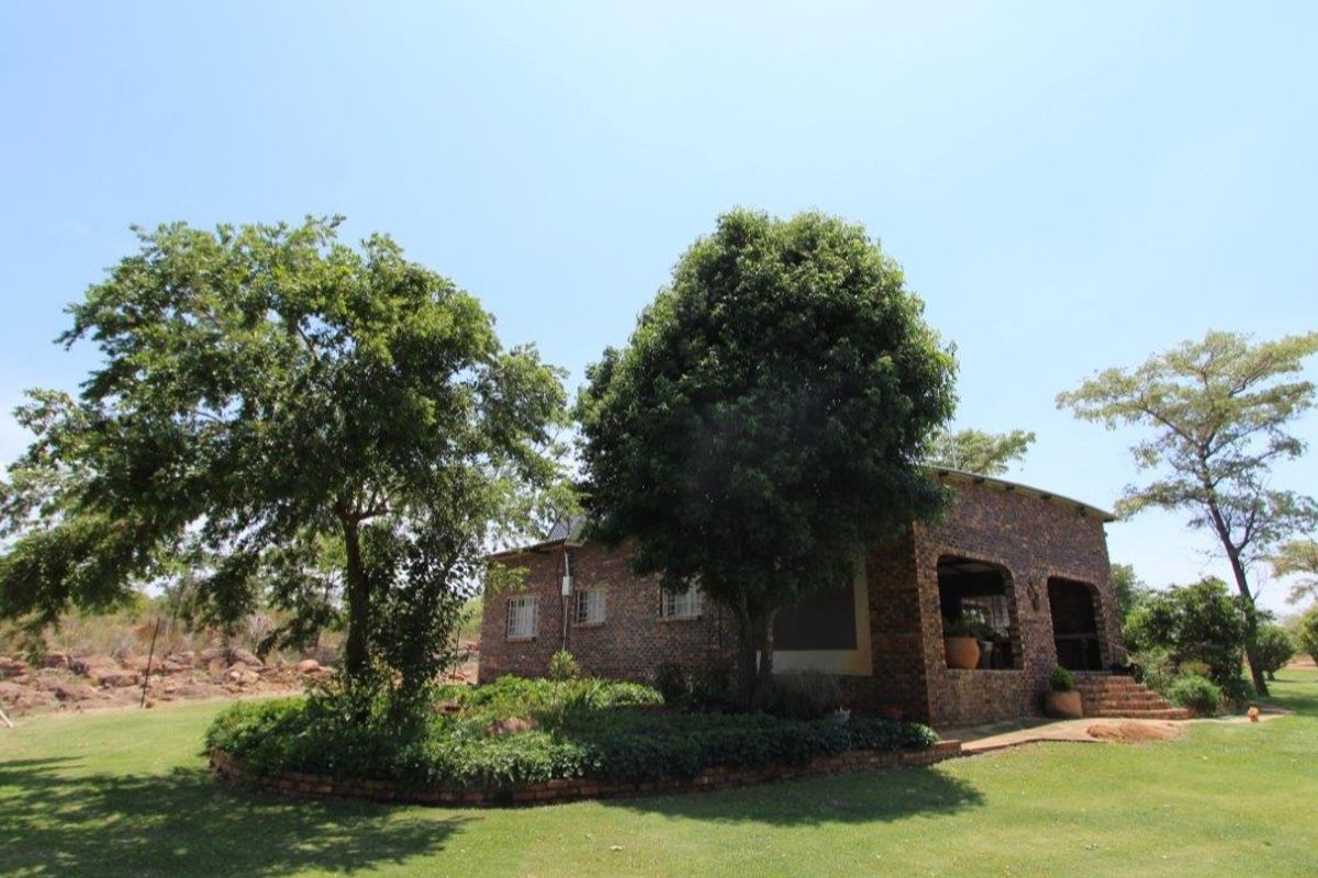 A view of the rear elevation of a face brick farm house featuring a covered patio and established garden surroundings.