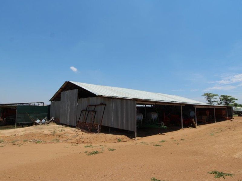 A large, open-sided agricultural utility shed with corrugated metal roofing and cladding, suitable for farm equipment storage.