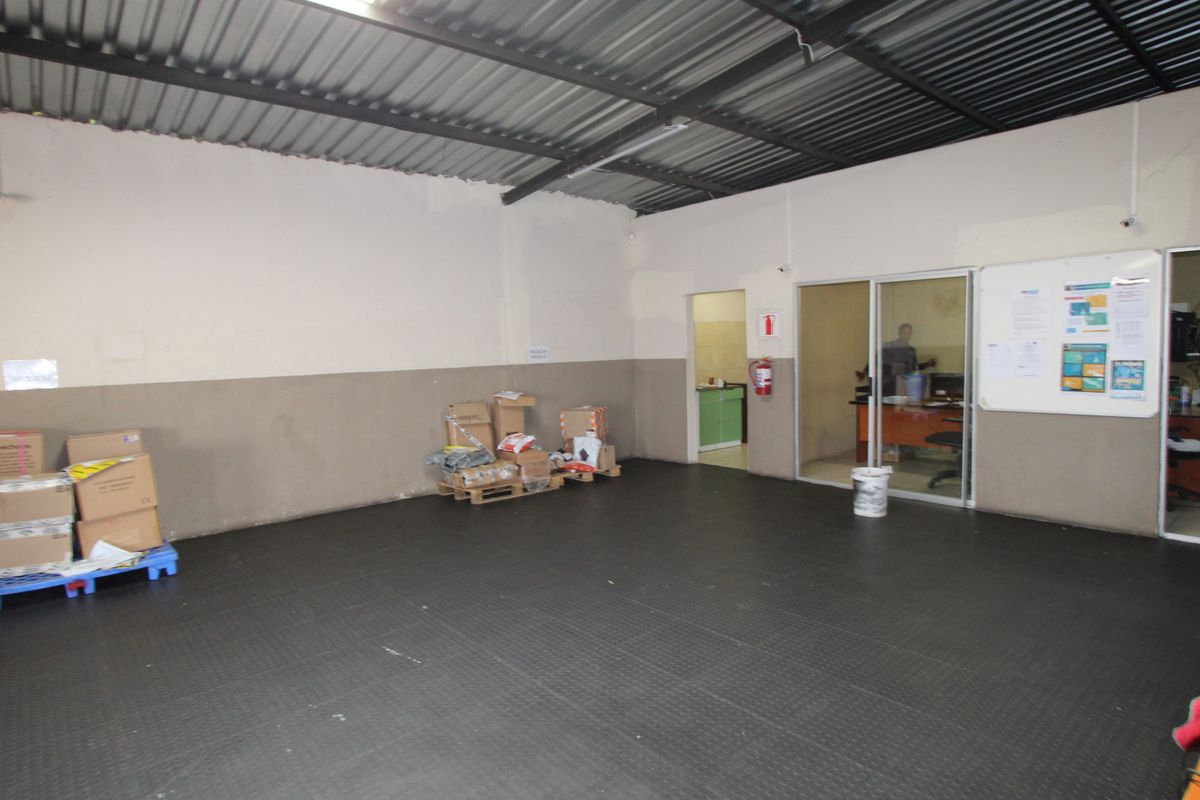 A functional utility or storage space featuring durable rubber flooring, exposed corrugated metal roofing, and a fire extinguisher, with an adjacent office area.