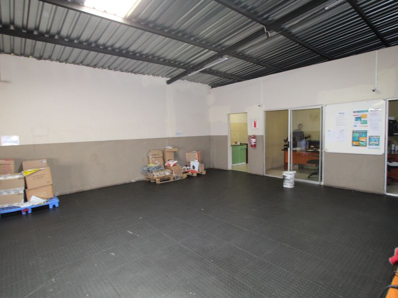 A functional utility or storage space featuring durable rubber flooring, exposed corrugated metal roofing, and a fire extinguisher, with an adjacent office area.