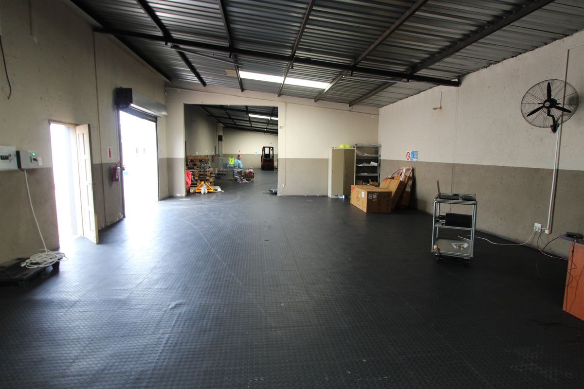 Spacious industrial utility area featuring durable rubberized flooring, high corrugated metal ceilings, and a wall-mounted industrial fan, suitable for storage or workshop use.