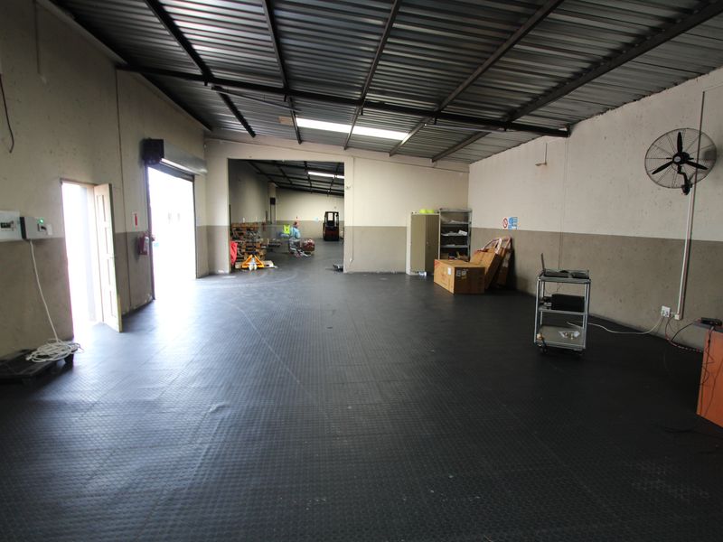 Spacious industrial utility area featuring durable rubberized flooring, high corrugated metal ceilings, and a wall-mounted industrial fan, suitable for storage or workshop use.