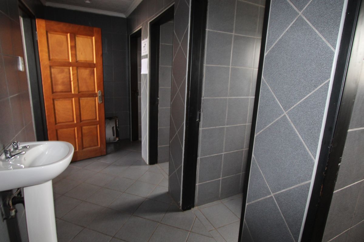 A functional commercial bathroom featuring tiled walls and flooring, a pedestal washbasin, and multiple private cubicle access points.