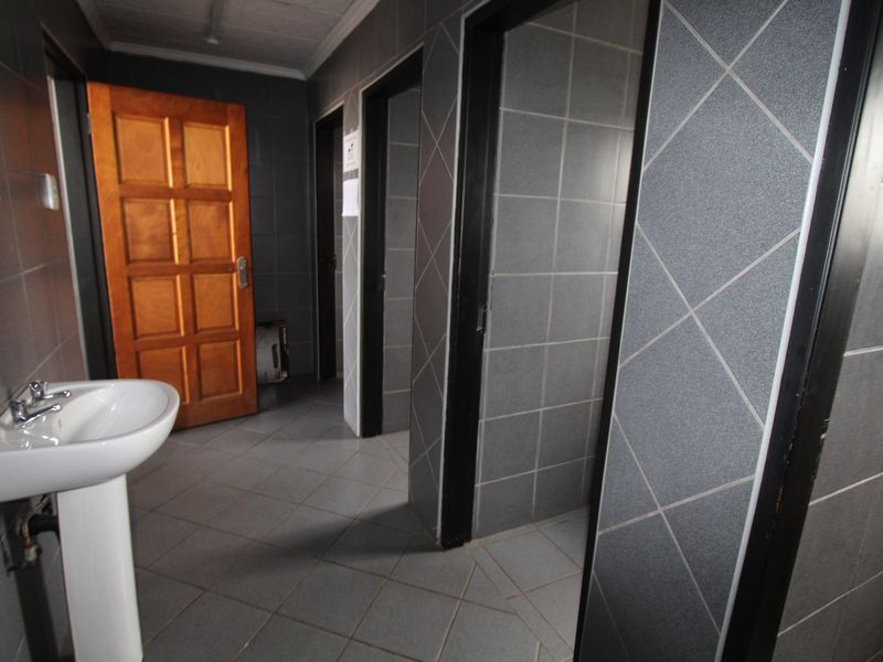 A functional commercial bathroom featuring tiled walls and flooring, a pedestal washbasin, and multiple private cubicle access points.