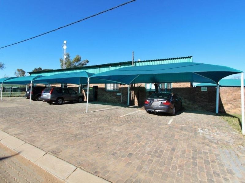 Exterior view of a business property featuring a paved parking area with multiple shade cloth carports and a brick building facade.