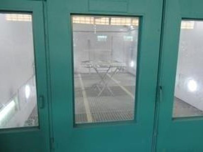 An industrial spray booth featuring metal grate flooring and glass-paneled access doors, designed for specialized commercial or automotive finishing tasks.