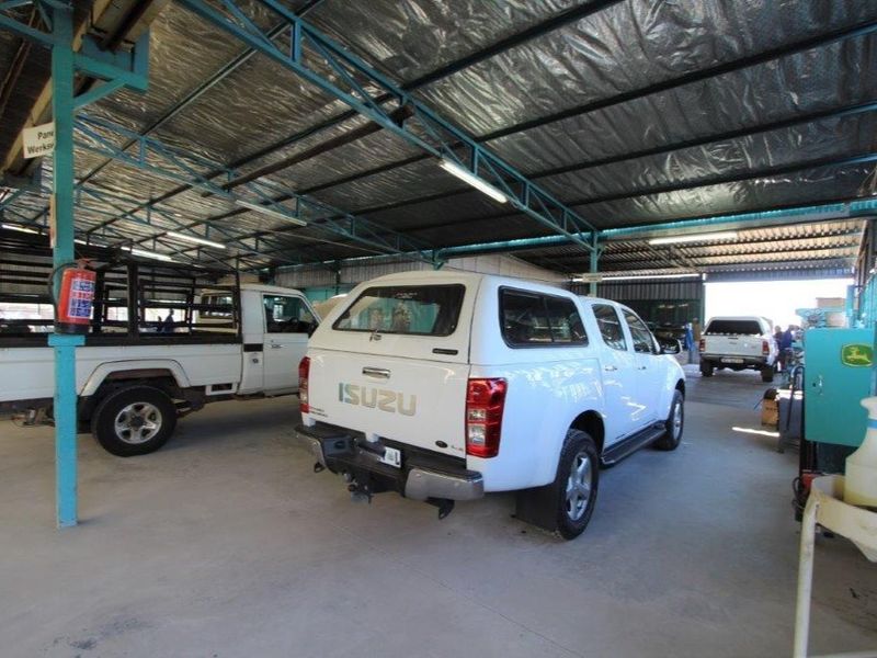 A spacious industrial garage or workshop area featuring a high metal roof structure, concrete flooring, and overhead fluorescent lighting.