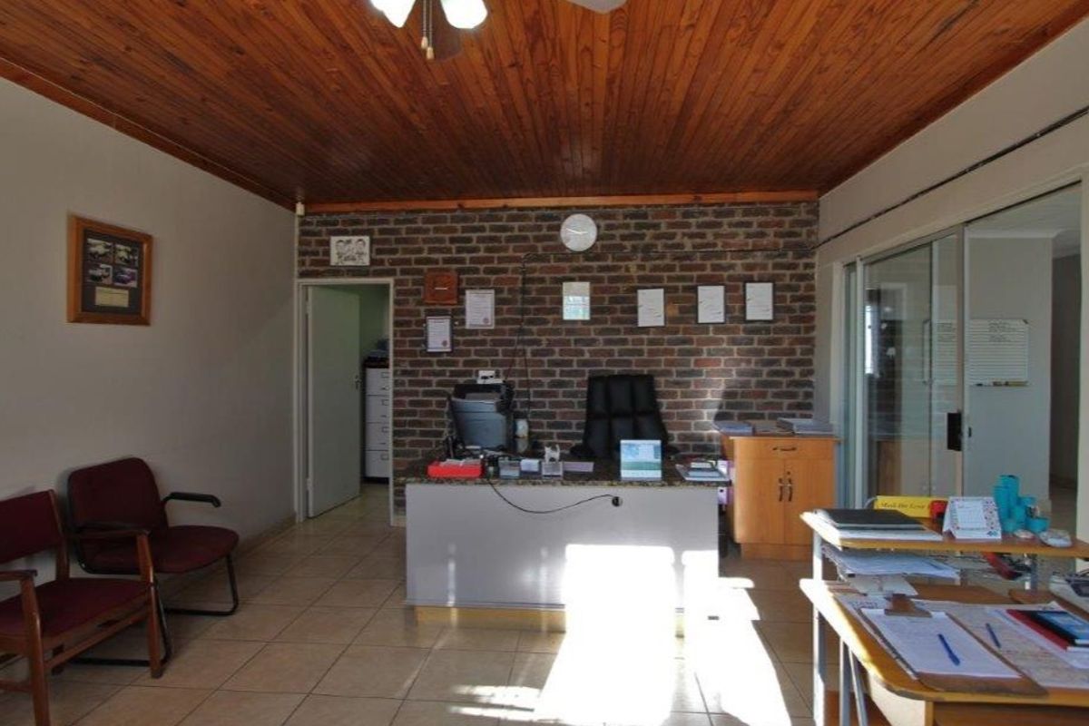 A functional office space featuring an exposed brick feature wall, timber ceiling, and tiled flooring, providing a professional work environment.