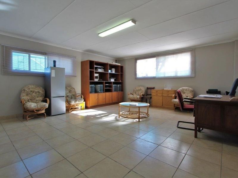 Spacious office area featuring neutral tiled flooring, large windows with venetian blinds, and overhead fluorescent lighting, suitable for a professional workspace.