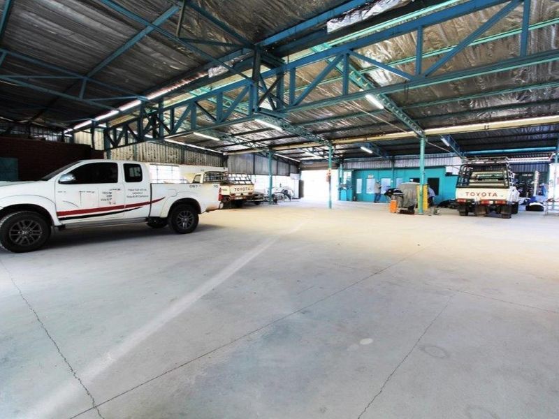 Spacious industrial garage or workshop area featuring exposed steel roof trusses, concrete flooring, and functional overhead lighting.