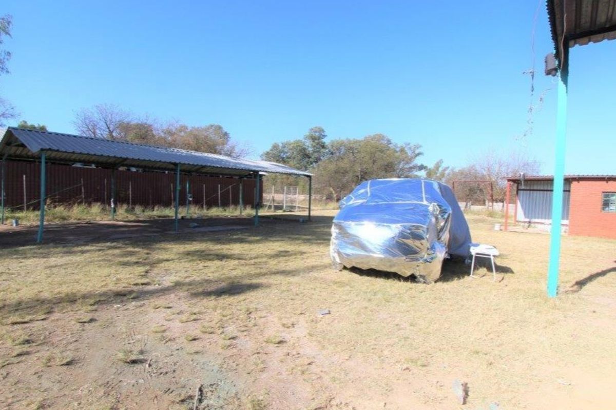 Outdoor area featuring a metal carport structure and a brick building, set on a large, undeveloped plot of land.