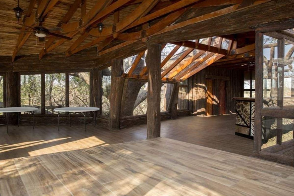 Spacious living area featuring rustic exposed timber roof trusses, large skylights, timber flooring, and a built-in bar, offering a unique architectural aesthetic.