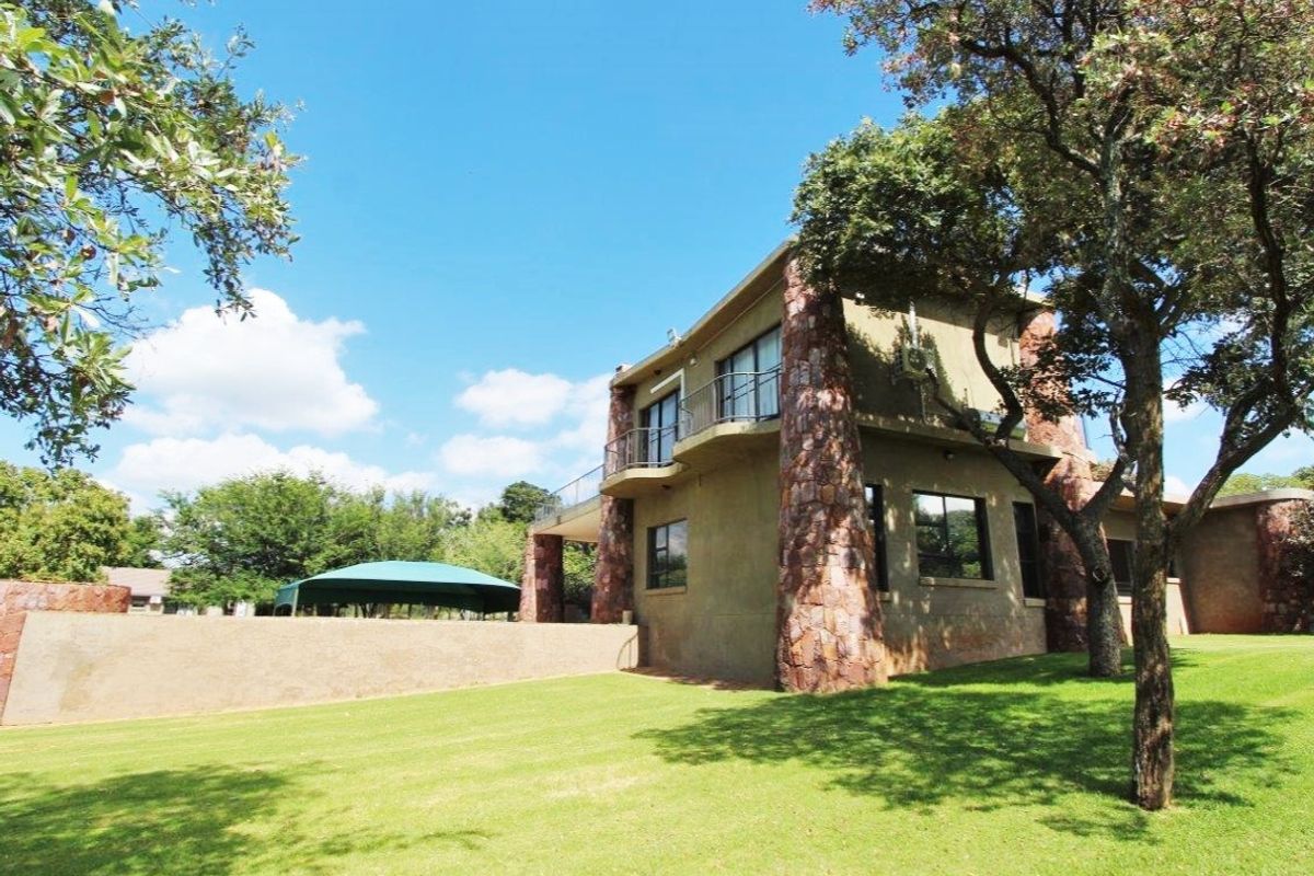Rear view of a multi-story farm residence featuring stone-clad pillars, a balcony with metal railings, and a well-maintained lawn.