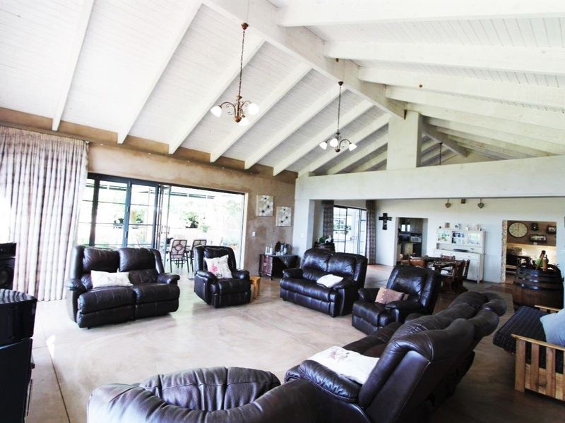 Spacious open-plan living area featuring high vaulted ceilings with exposed timber rafters, polished concrete floors, and large sliding glass doors leading to the patio.