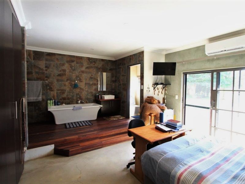 Spacious bedroom featuring an integrated open-plan bathroom area with a raised wooden platform, freestanding bathtub, and modern vanity, complemented by sliding glass door access.