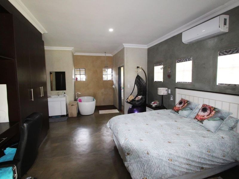 Spacious bedroom featuring polished concrete floors, an integrated en-suite bathroom with a freestanding tub, built-in cabinetry, and a wall-mounted air conditioning unit.