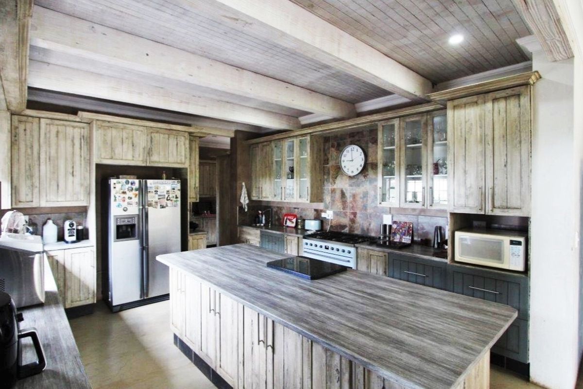 Spacious farmhouse kitchen featuring a large central island, rustic timber cabinetry, exposed ceiling beams, and stone tile backsplash with integrated appliances.