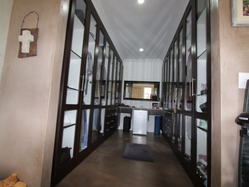 A spacious walk-in dressing room featuring extensive floor-to-ceiling glass-fronted built-in cabinetry and a central vanity area with recessed lighting.