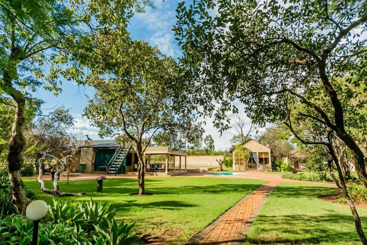 Spacious farm property featuring a well-maintained garden, brick pathways, a swimming pool, and a covered patio area with an external staircase.
