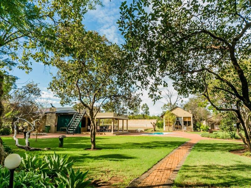 Spacious farm property featuring a well-maintained garden, brick pathways, a swimming pool, and a covered patio area with an external staircase.