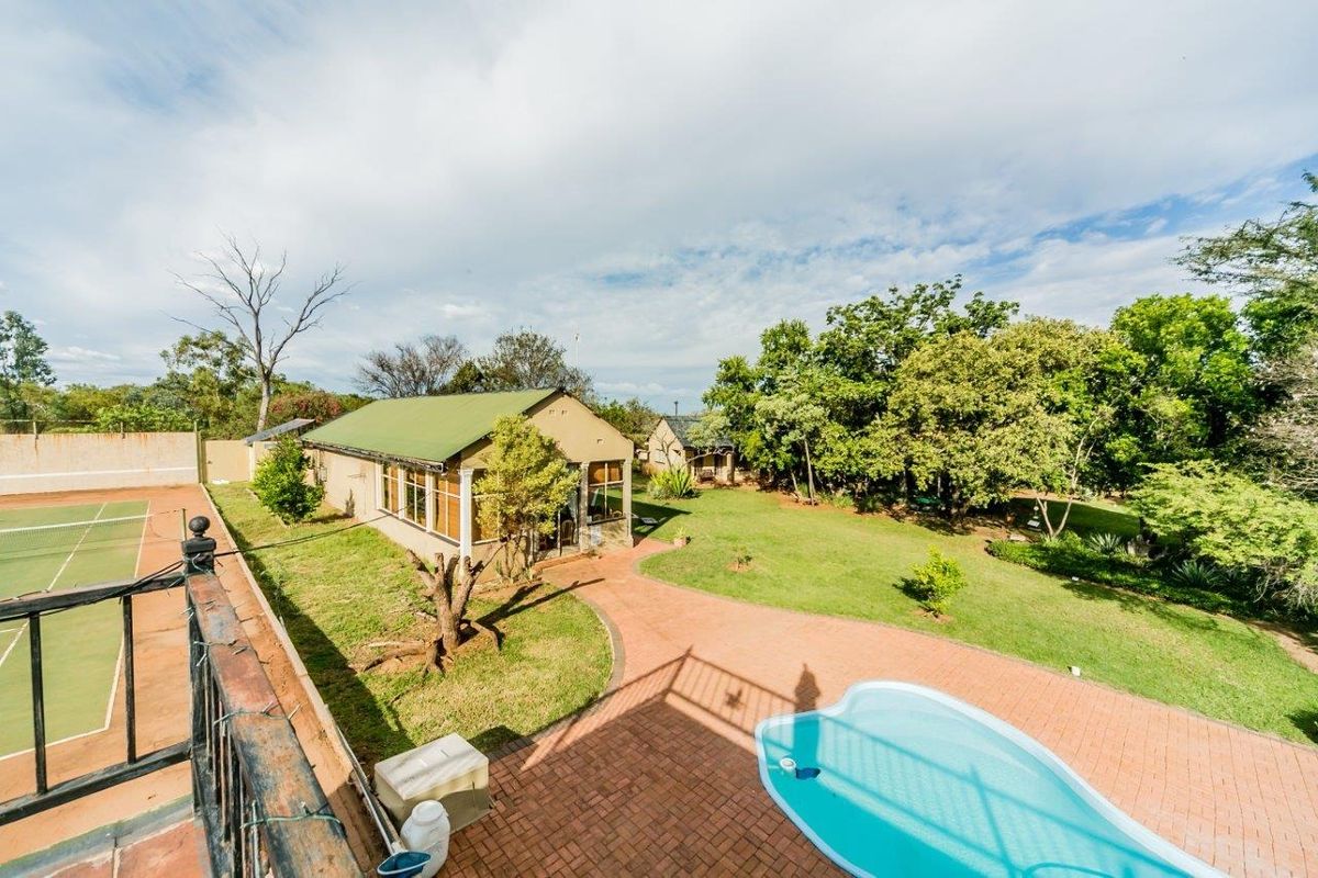 Aerial view of the property grounds featuring a swimming pool, tennis court, paved patio areas, and established garden surroundings.