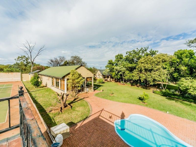 Aerial view of the property grounds featuring a swimming pool, tennis court, paved patio areas, and established garden surroundings.