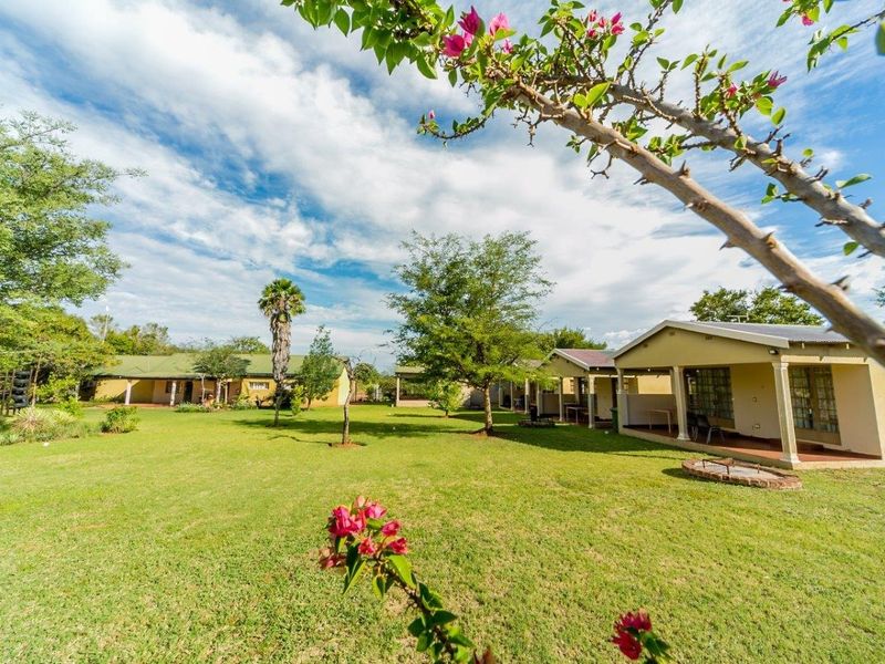 A spacious rear garden area featuring a well-maintained lawn, mature trees, and covered patio spaces attached to the farm buildings.