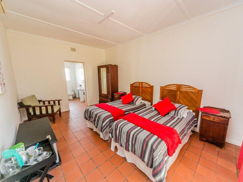 A functional bedroom featuring terracotta tile flooring, an en-suite bathroom, and a wall-mounted air conditioning unit.