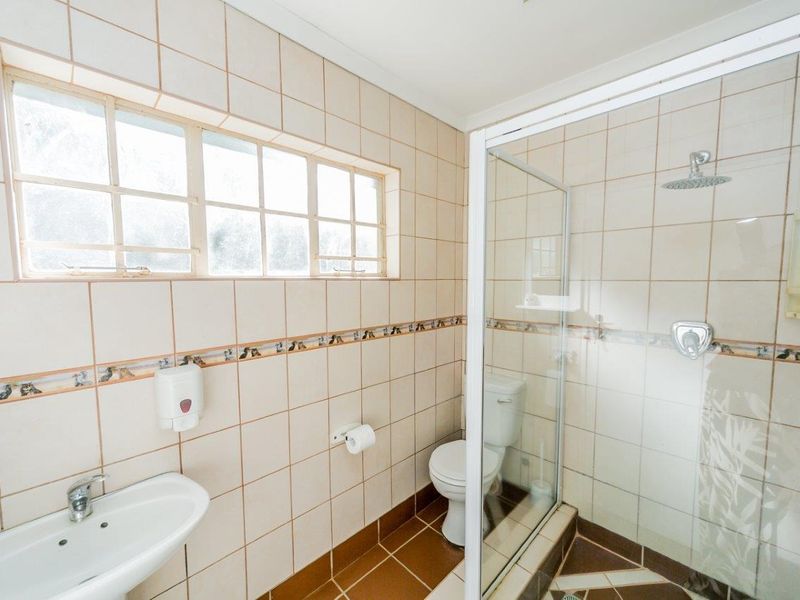 A functional bathroom featuring a shower enclosure, wall-mounted basin, toilet, and neutral tiled finishes throughout.
