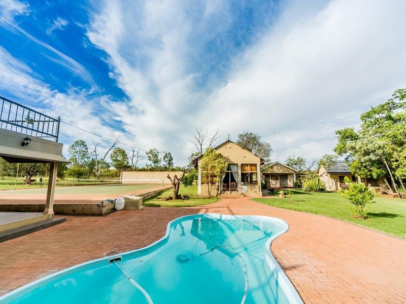 Outdoor entertainment area featuring a swimming pool, brick paved patio, and a tennis court set within a spacious garden landscape.