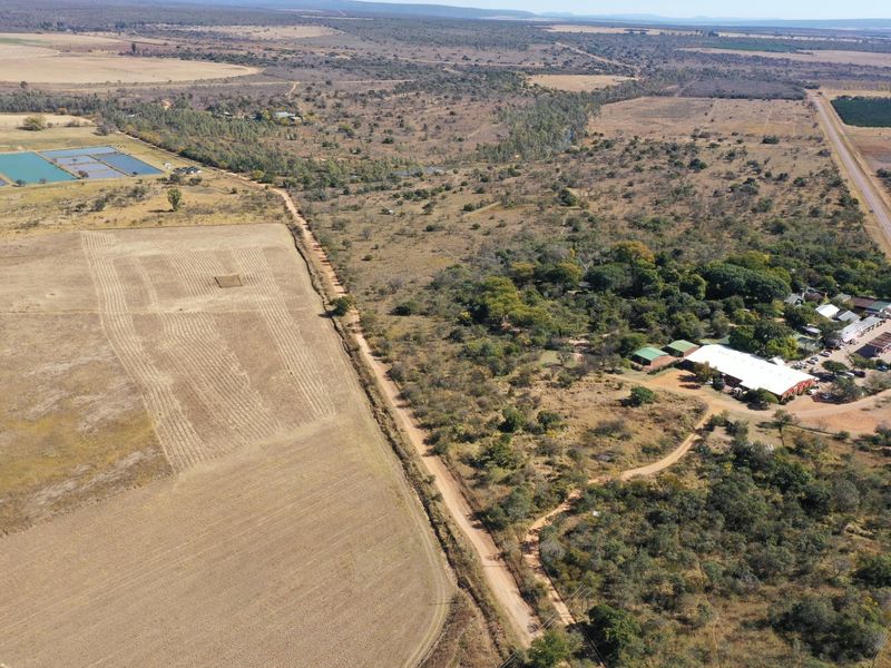Aerial view of a rural property featuring a commercial building complex, extensive agricultural land, and unpaved access roads in a natural landscape setting.